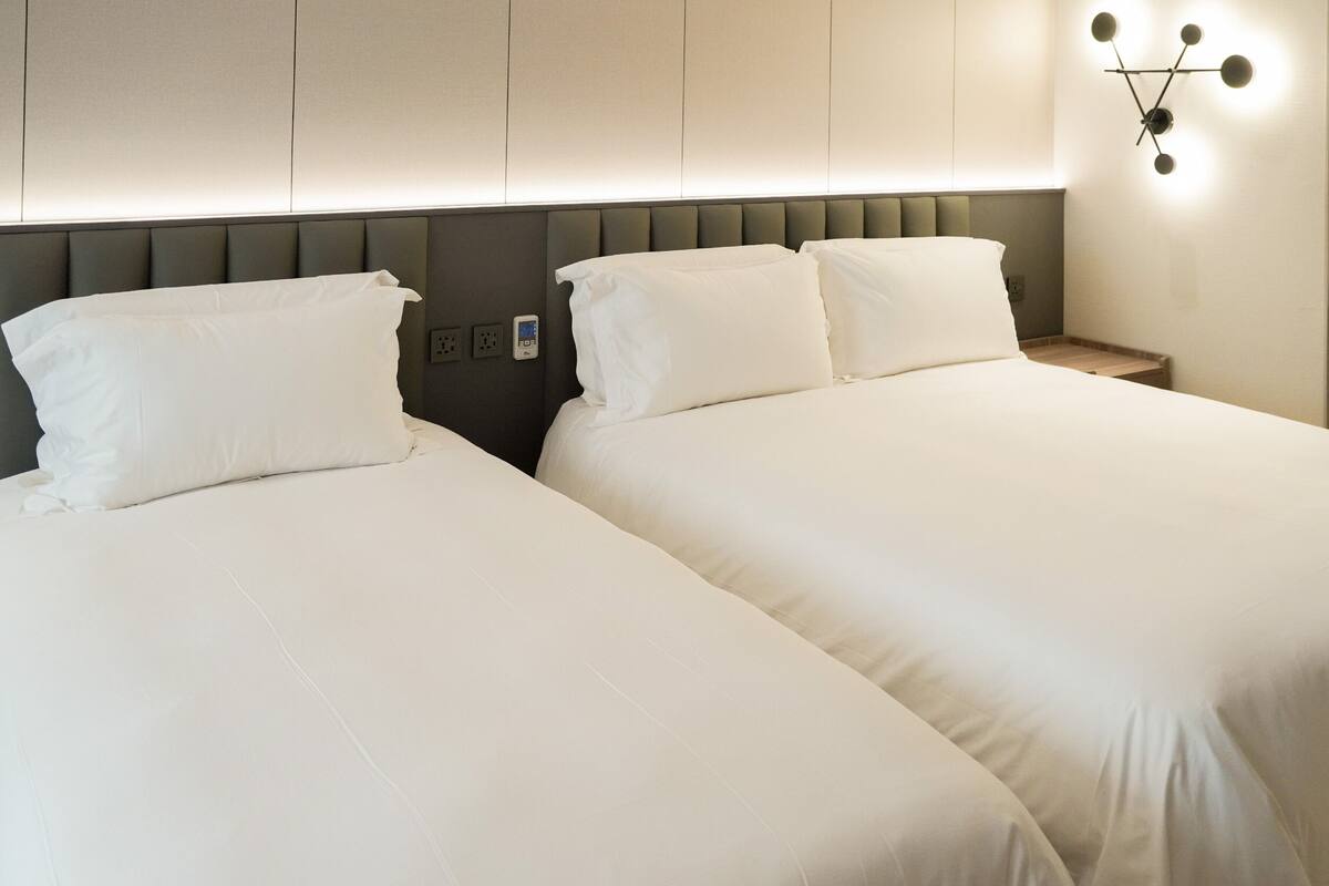 Une chambre d’hôtel avec deux lits, une tête de lit moderne et un luminaire fixé au mur.