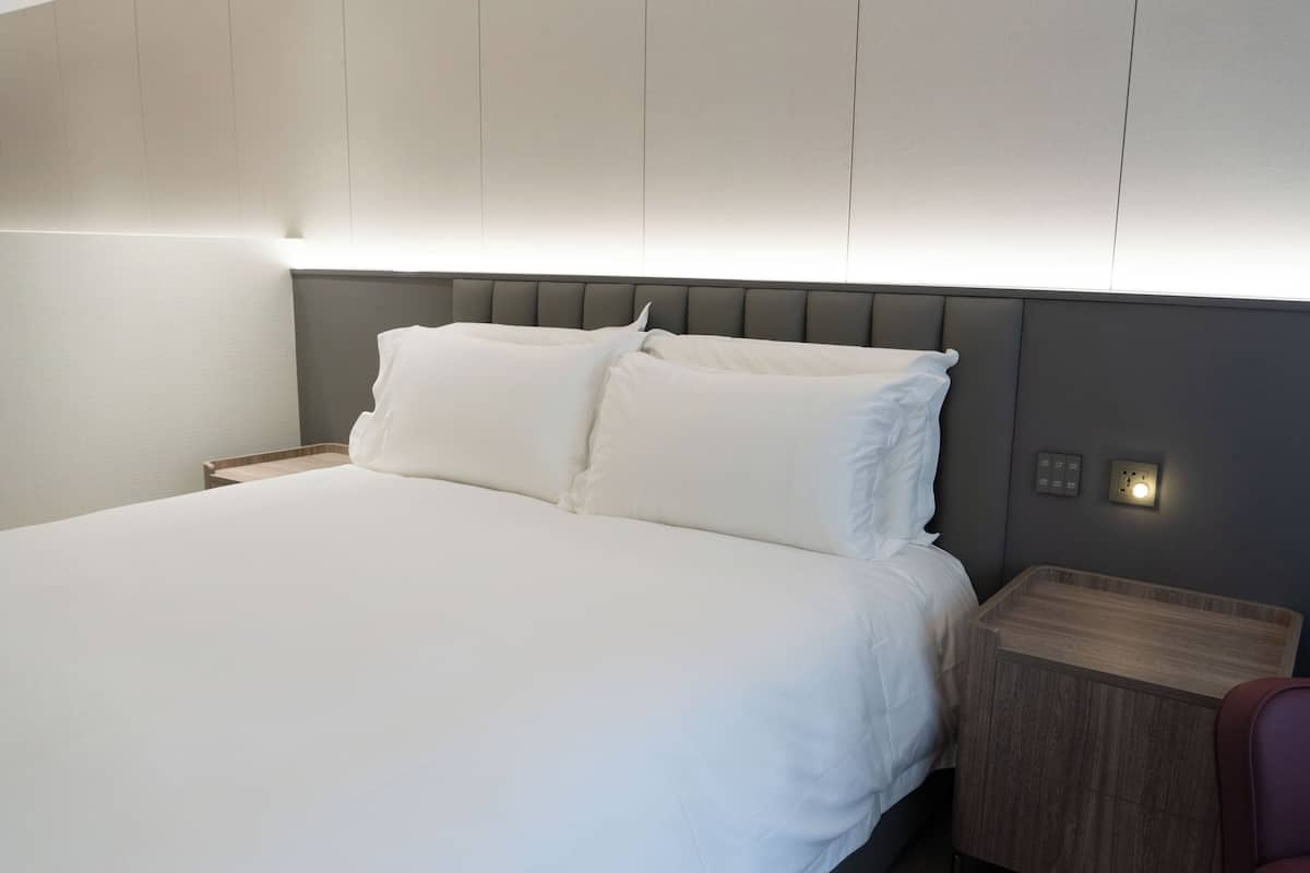 Un lit bien fait, avec du linge de lit blanc, une table de chevet en bois et une tête de lit moderne.