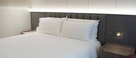 A neatly made bed with white linens, a wooden nightstand, and a modern headboard.
