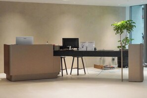 A modern office space with a desk, computer, and two stools. There is a plant and a large window in the background. - TALMUD HOTEL CLASSIC TAIWAN BOULEVARD (Taichung)