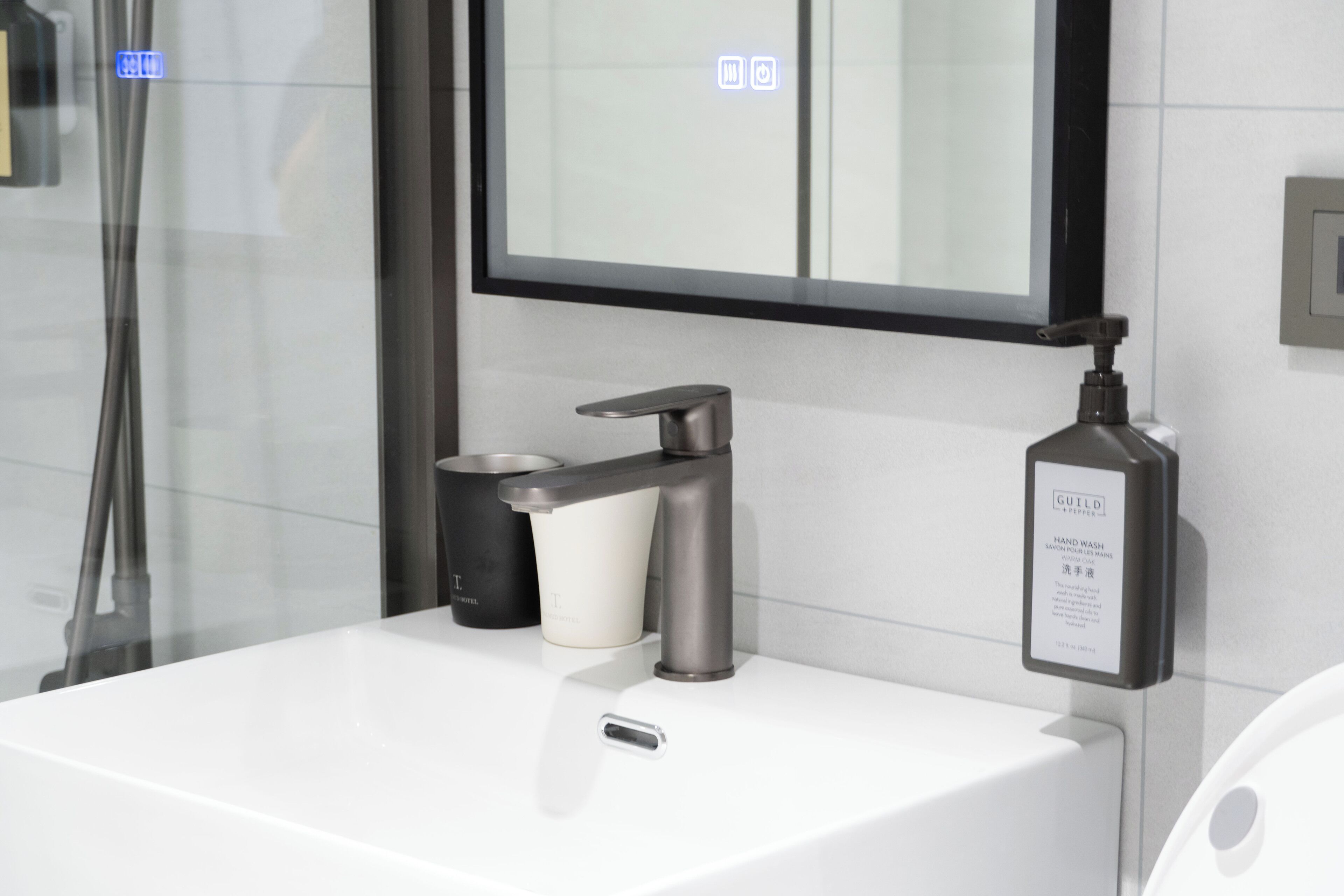 A modern bathroom with a white sink, a faucet, and a hand soap dispenser.