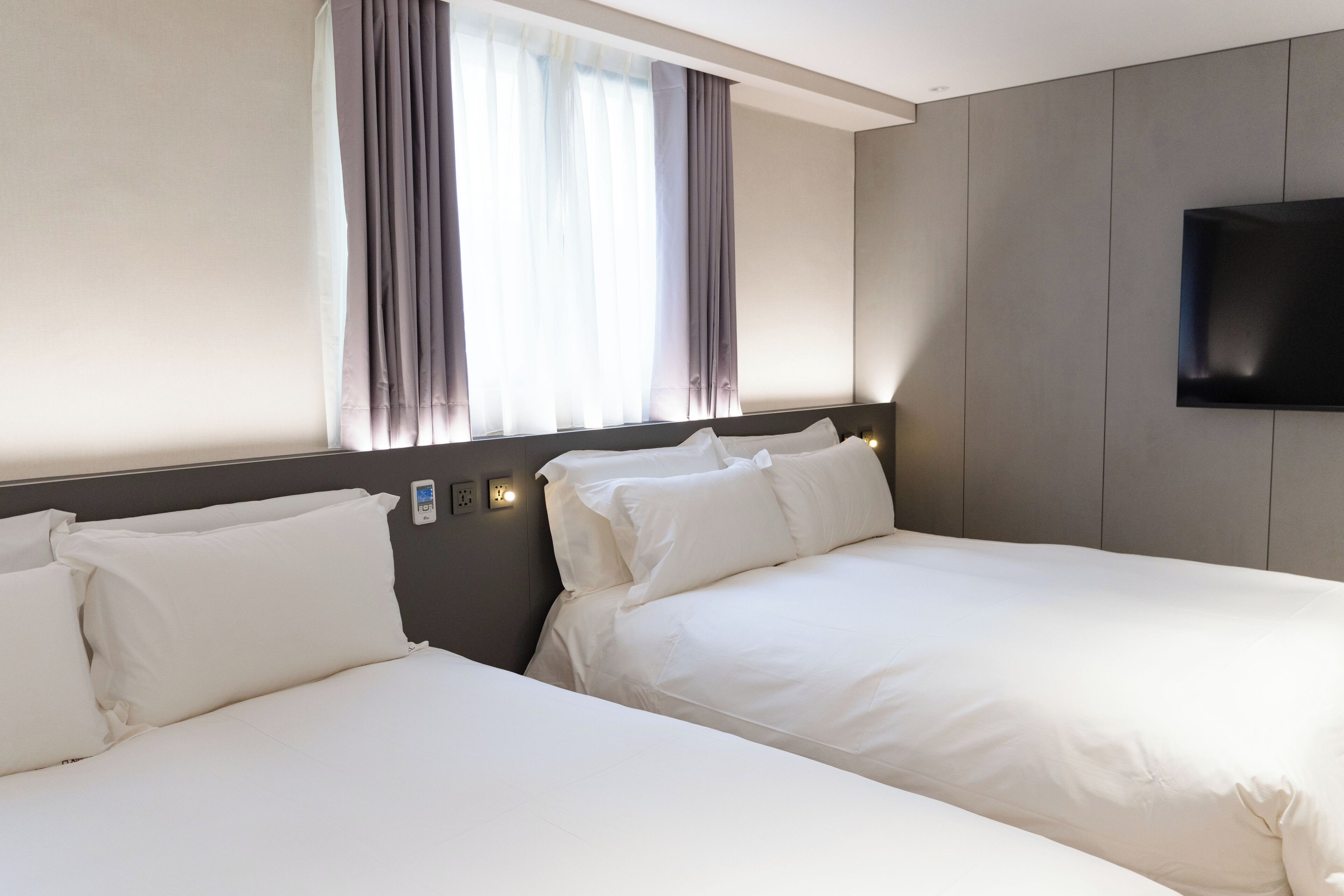 Quarto de hotel com duas camas, televisão de tela plana na parede e janela com cortinas.