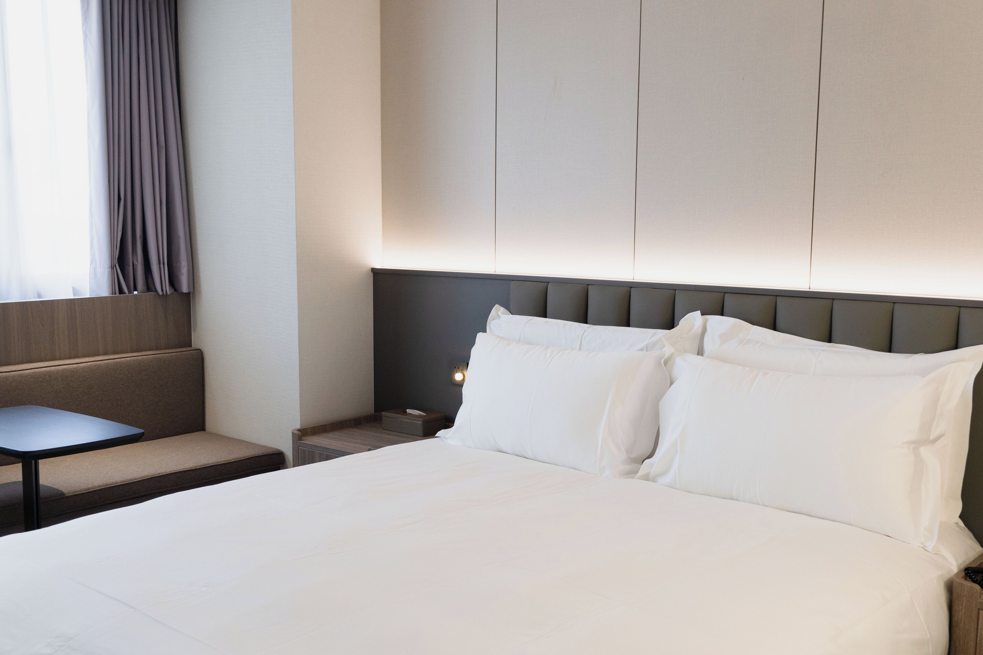 Une chambre d’hôtel avec un grand lit, une petite table, un banc et une table de chevet avec une lampe.