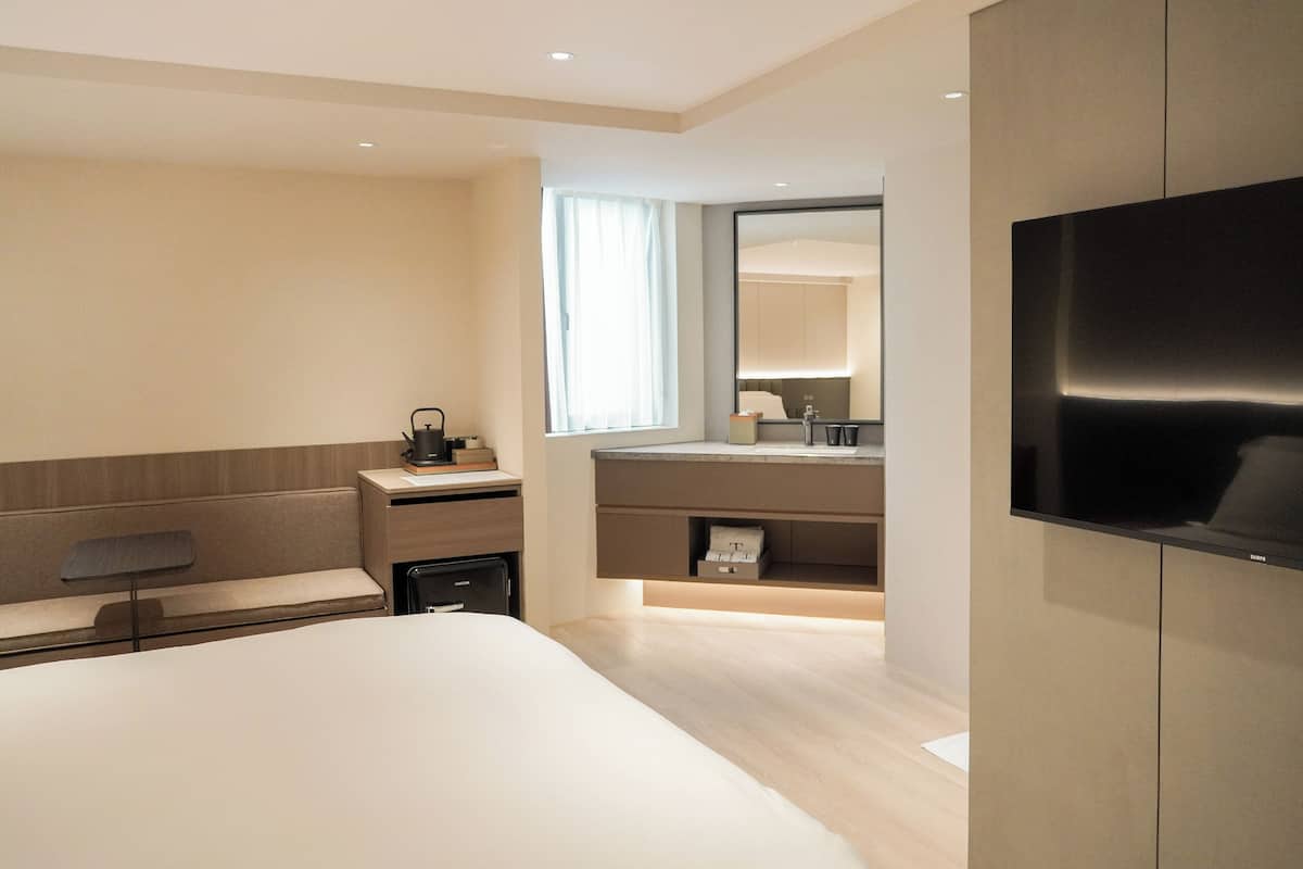 Une chambre d’hôtel moderne dotée d’un grand lit, d’un bureau avec une chaise, d’une coiffeuse avec un miroir et d’un téléviseur à écran plat fixé au mur.