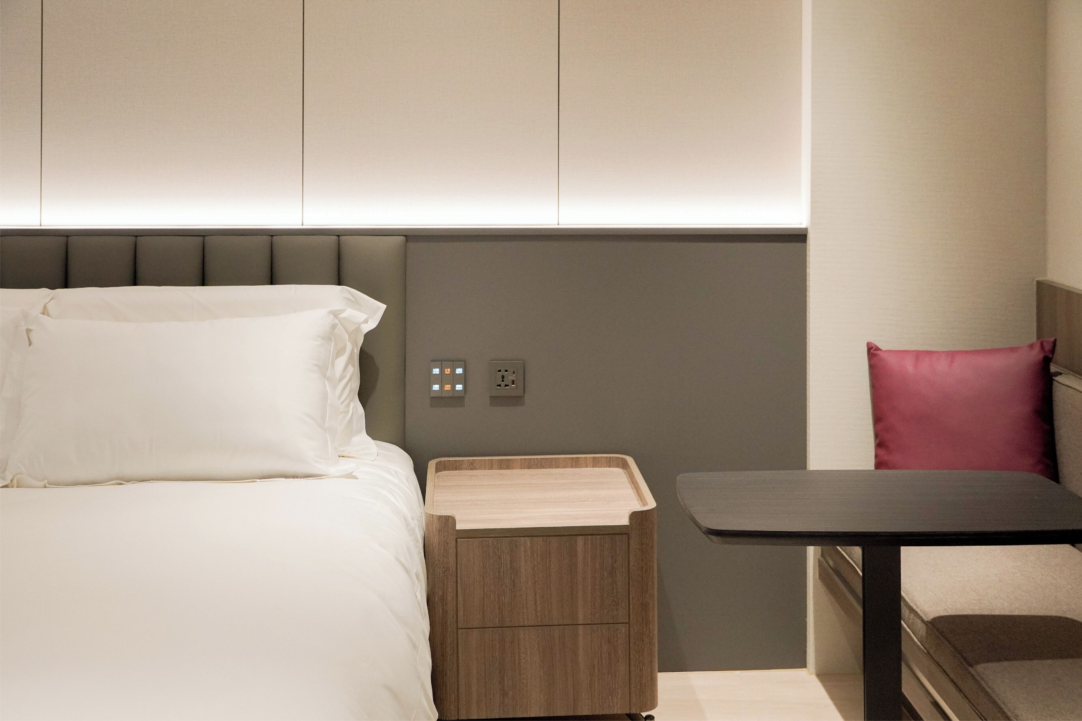 Habitació d'hotel moderna amb un llit, una taula de nit i una petita taula auxiliar de fusta.