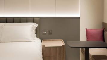 Habitació d'hotel moderna amb un llit, una taula de nit i una petita taula auxiliar de fusta.