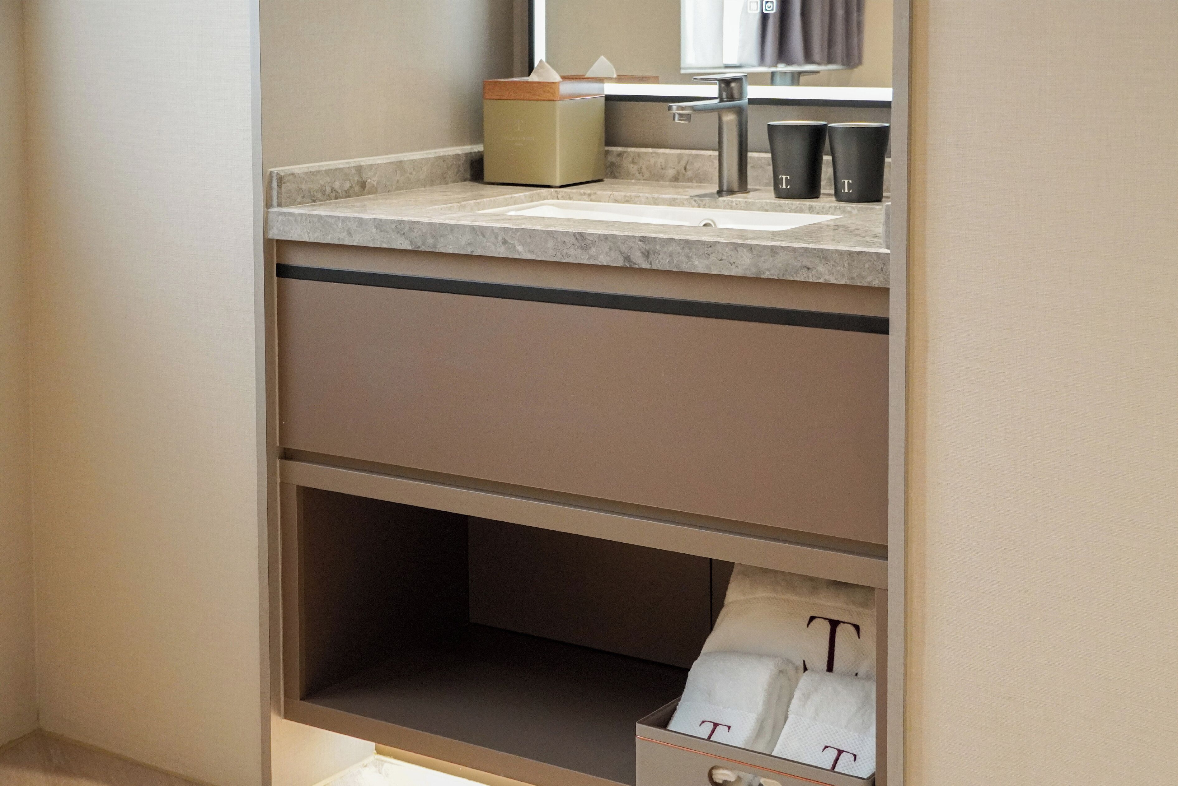 A bathroom with a sink, towel dispenser, and storage cabinet.