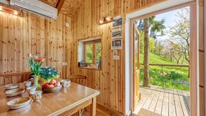 Un interior de madera con una mesa de comedor dispuesta, un espejo y vistas a un jardín a través de una puerta de vidrio.