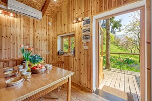 A wooden interior with a dining table set, a mirror, and a view of a garden through a glass door.