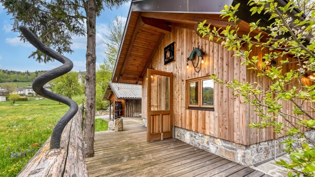 Una cabaña de madera con un porche de madera, cimientos de piedra y un letrero que dice 'Welcome'.