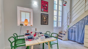 Un coin repas avec une table dressée pour quatre personnes, des chaises vertes, une lampe de table allumée et des œuvres d’art accrochées aux murs.