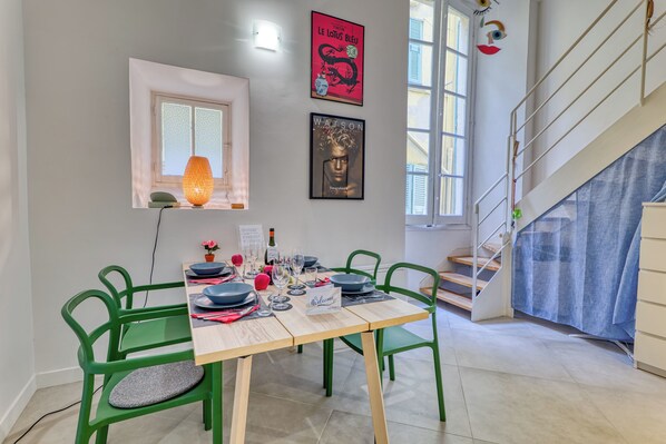 A dining area with a table set for four, green chairs, a lit table lamp, and artwork on the walls.