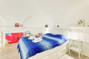 A bedroom with a bed, a desk, a chair, and a painting on the wall.