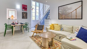 Un salon moderne comprenant un canapé, une table à manger avec des chaises, un escalier et une grande fenêtre.