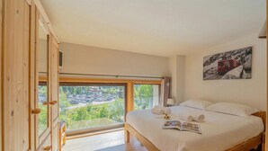 A bedroom with a large window, wooden wardrobe, a bed with white linens, and a painting on the wall. - Grand Roc A215 150m from Slopes, Mountain View & Parking, Argentière (Chamonix), France (Argentière (Chamonix))
