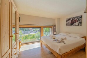 Ein Schlafzimmer mit großem Fenster, einem Holzschrank, einem Bett mit weißer Bettwäsche und einem Bild an der Wand.