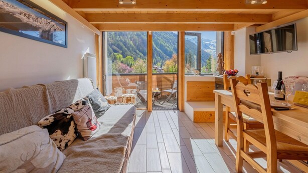A cozy room with a wooden ceiling, a sofa, a dining table, and a view of mountains through large windows. - Grand Roc A215 150m from Slopes, Mountain View & Parking, Argentière (Chamonix), France (Argentière (Chamonix))