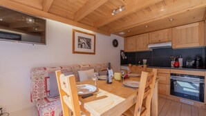 A cozy kitchen with wooden cabinets, a dining table set for two, and a built-in oven. - Grand Roc A215 150m from Slopes, Mountain View & Parking, Argentière (Chamonix), France (Argentière (Chamonix))