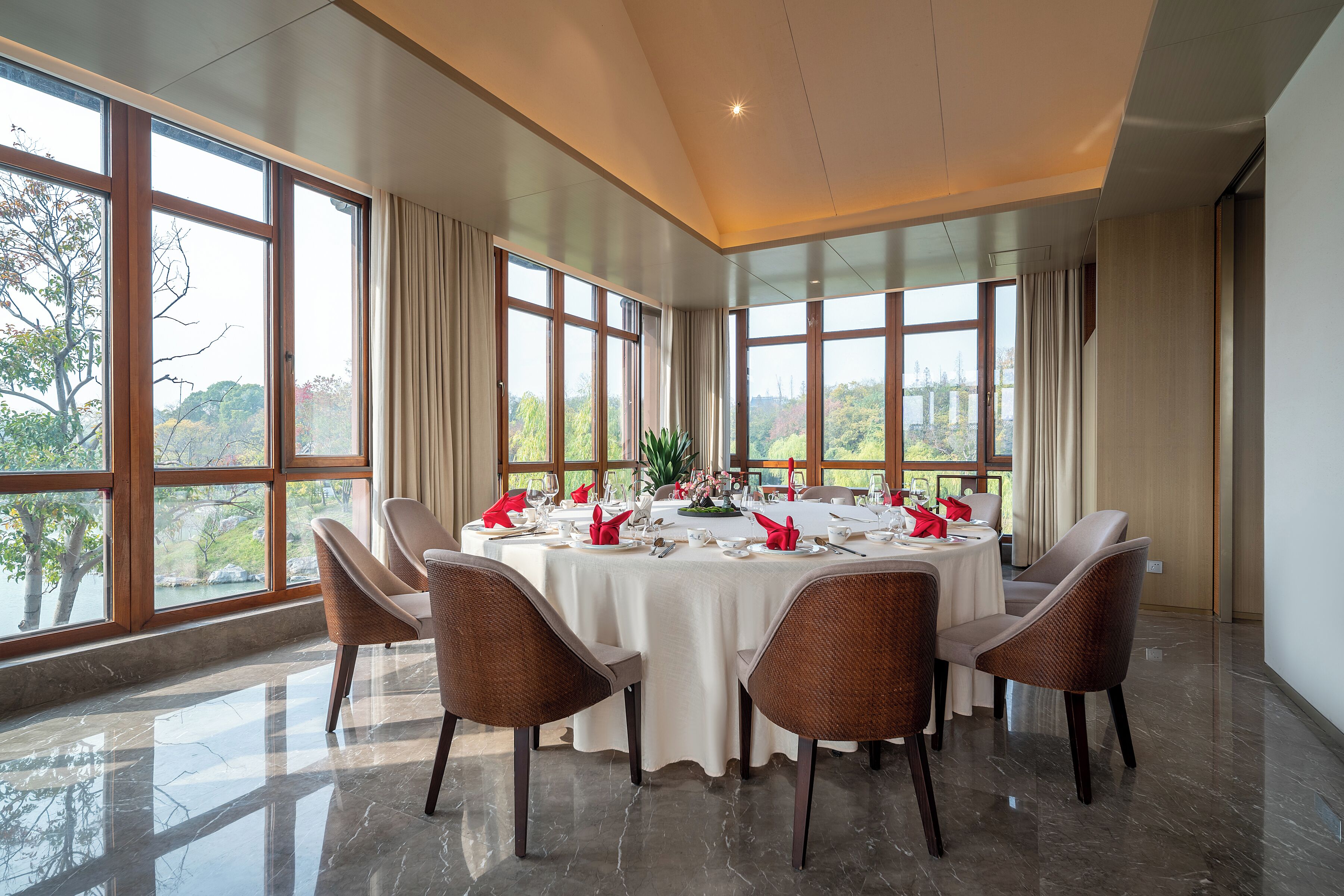 A dining area with a round table set for six, large windows, and a view of greenery.