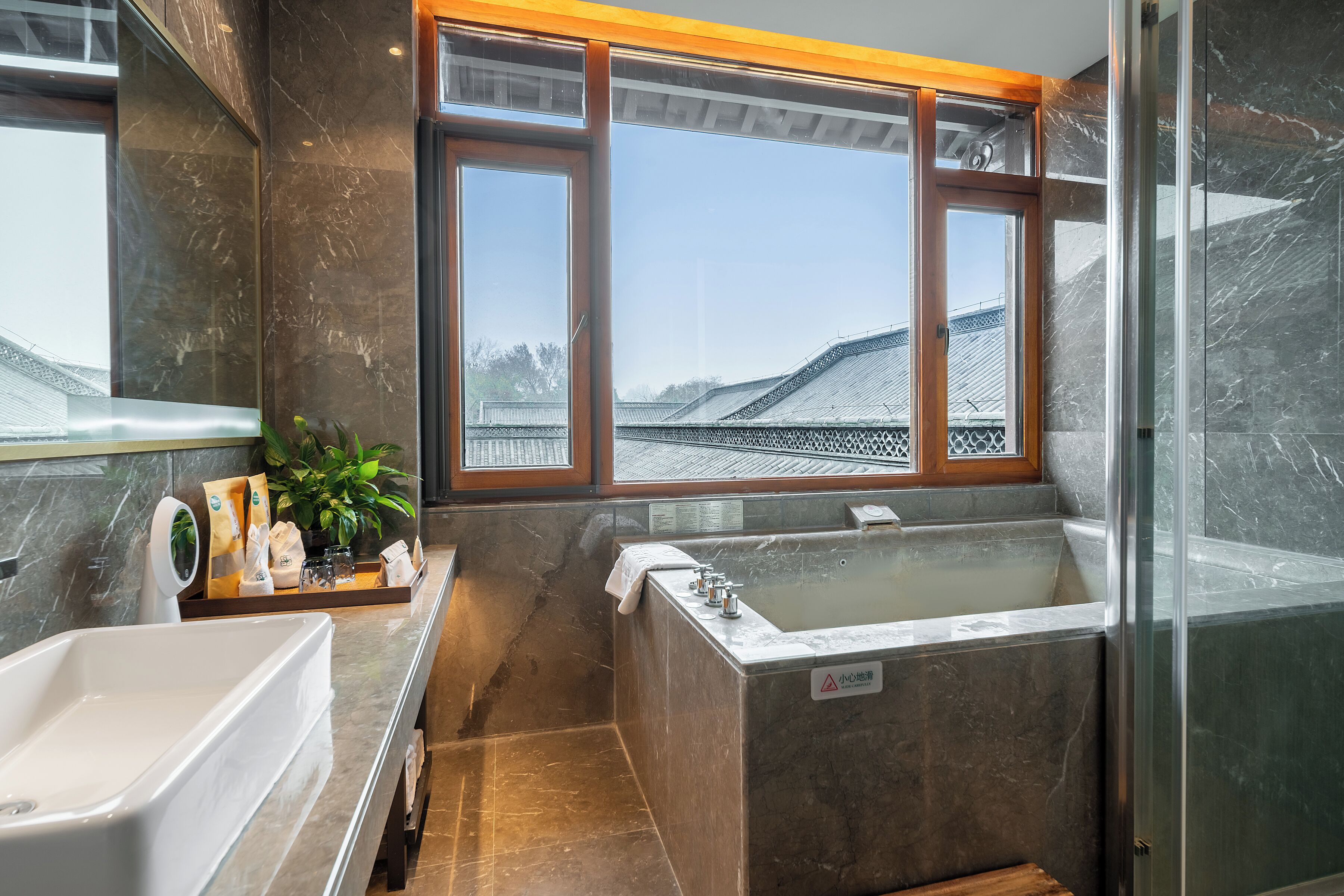 Un baño moderno con una bañera grande, un lavamanos y una ducha. Se aprecia una ventana con vistas a edificios.