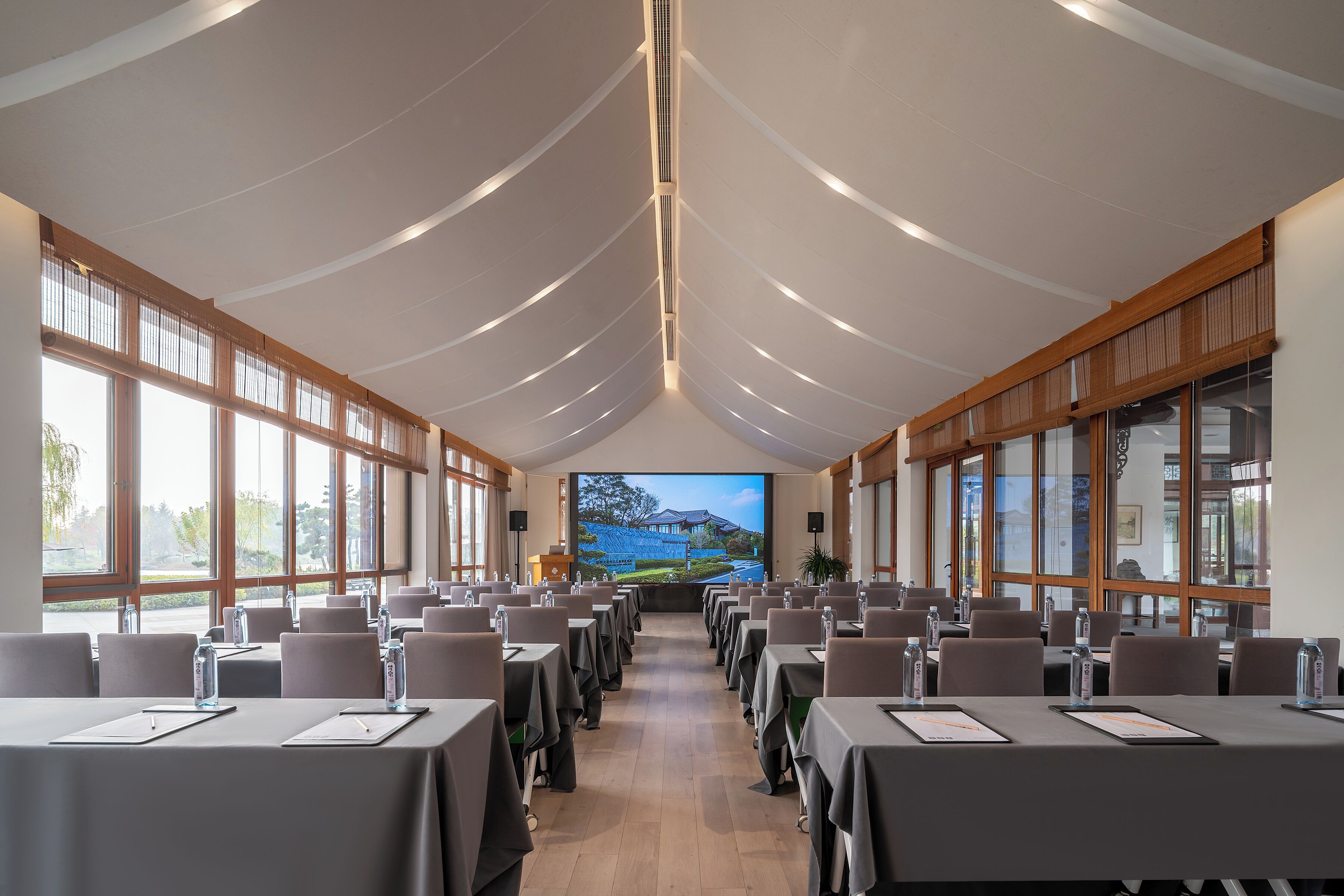 Un salón de conferencias con mesas, sillas y una pantalla grande que muestra una vista panorámica.