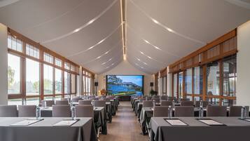 Un salón de conferencias con mesas, sillas y una pantalla grande que muestra una vista panorámica.