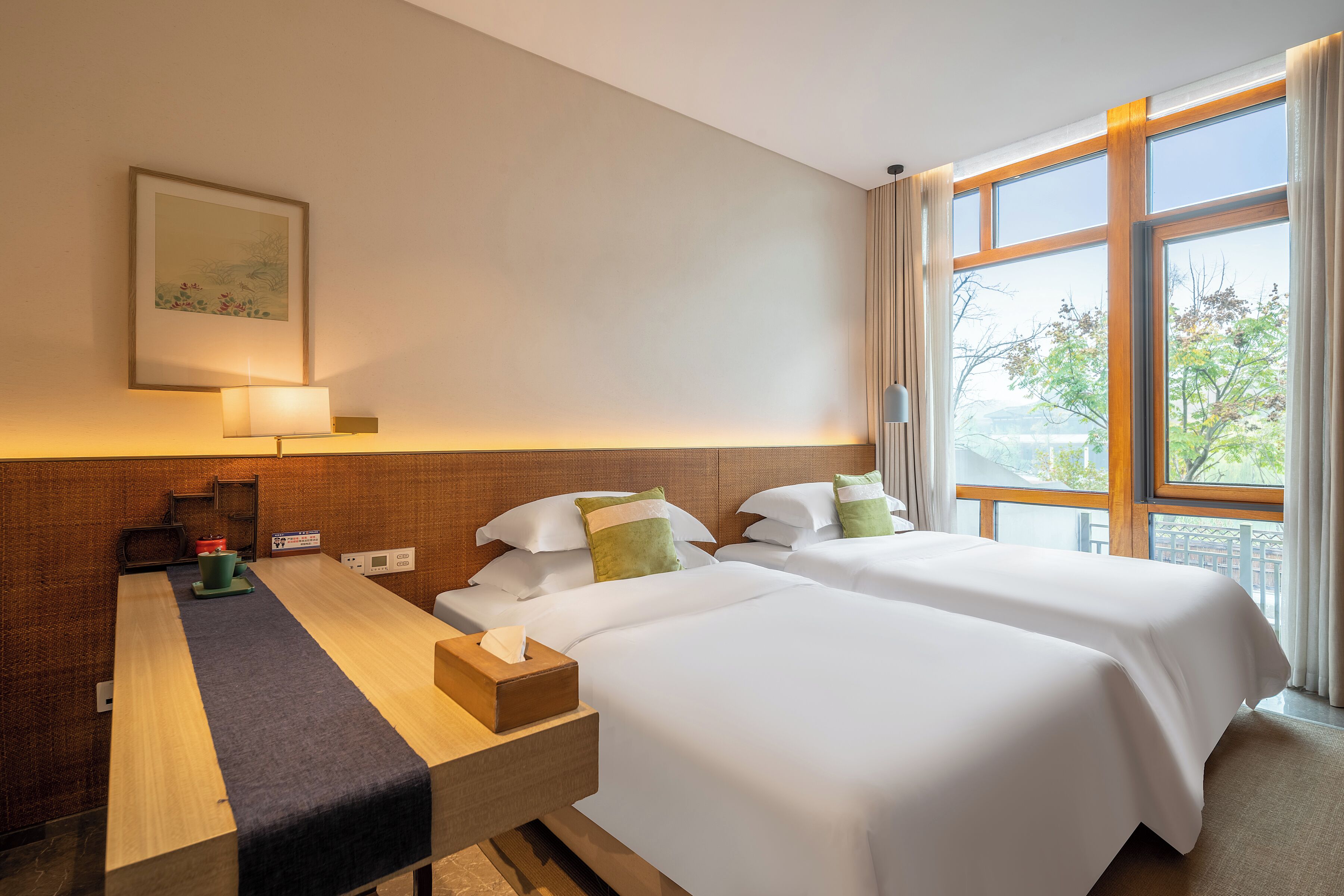 A hotel room with two beds, a desk, a lamp, and a window with a view.