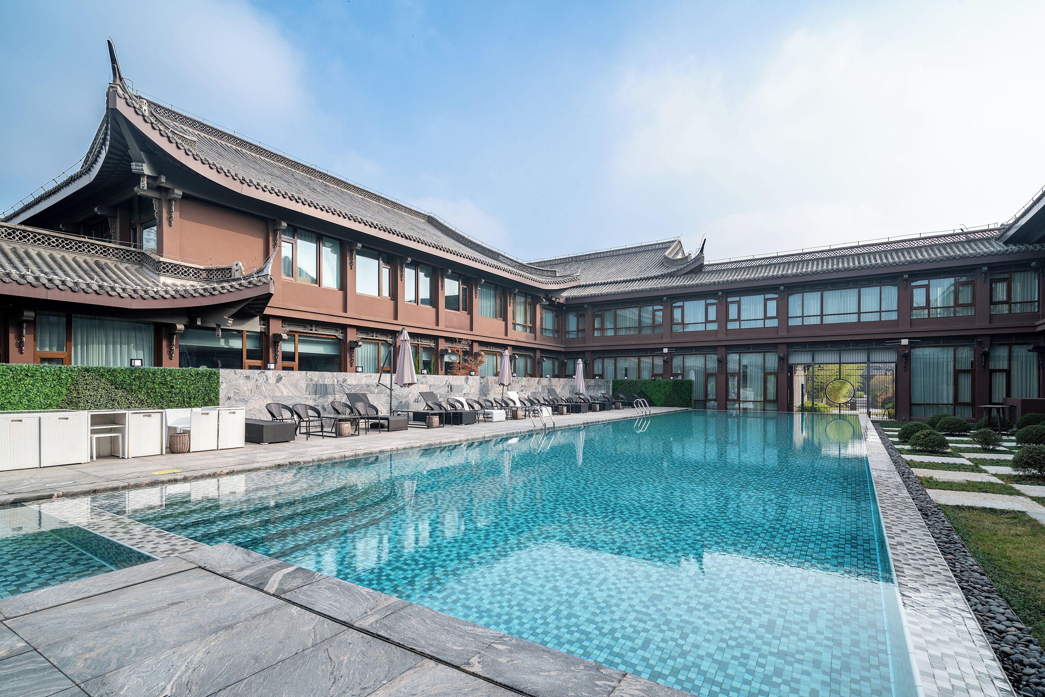 A traditional building with a swimming pool, lounge chairs, and a well-maintained garden.