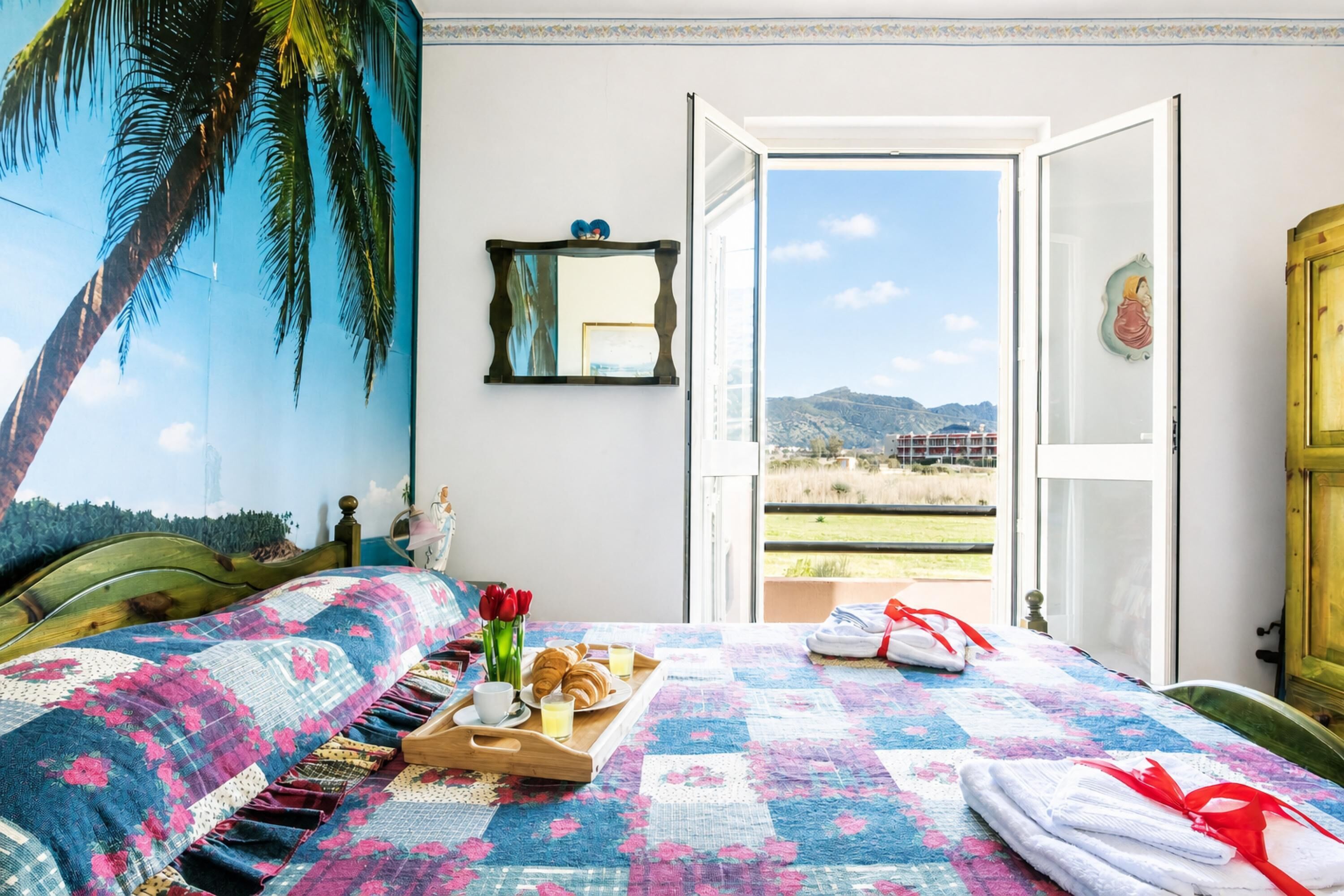 A room with a bed, a window, a door, and a view of the outdoors.
