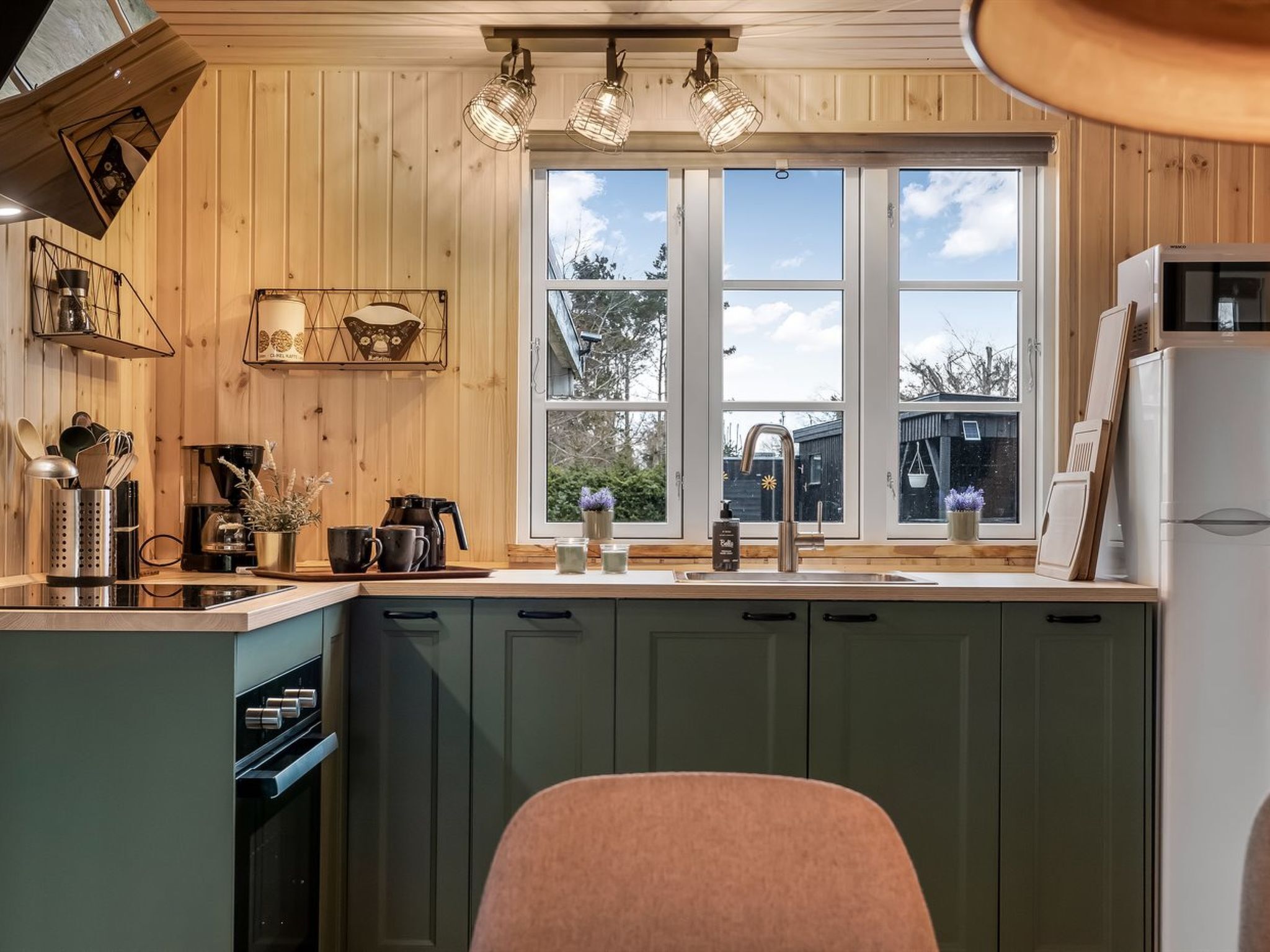 Una cocina con paredes de madera, una ventana, un lavamanos y un refrigerador.