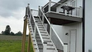 Un edificio de dos pisos con fachada blanca, un balcón en el piso superior y una escalera que conduce a la entrada.