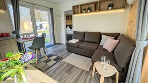 A modern living room with a sofa, a small table, a dining area with a vase of flowers, and a view through the glass door. - Beautiful apartment in villa for 4 people with WIFI and TV (Beilngries)