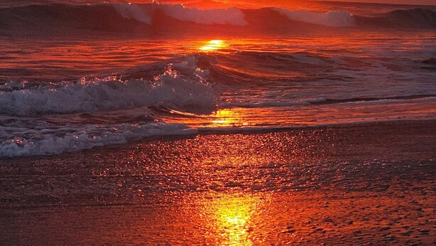 Un coucher de soleil sur l’océan, avec des vagues qui déferlent sur le rivage.