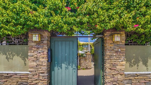 A stone-arched entrance with a green door, leading to a pathway.