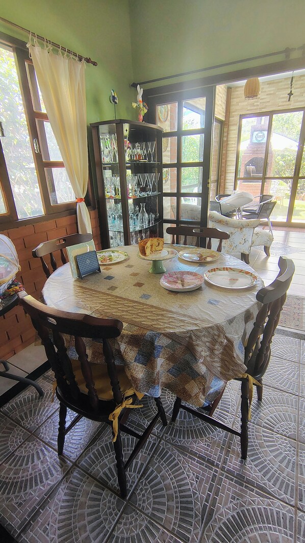A dining area with a round table covered by a patterned tablecloth, surrounded by wooden chairs.