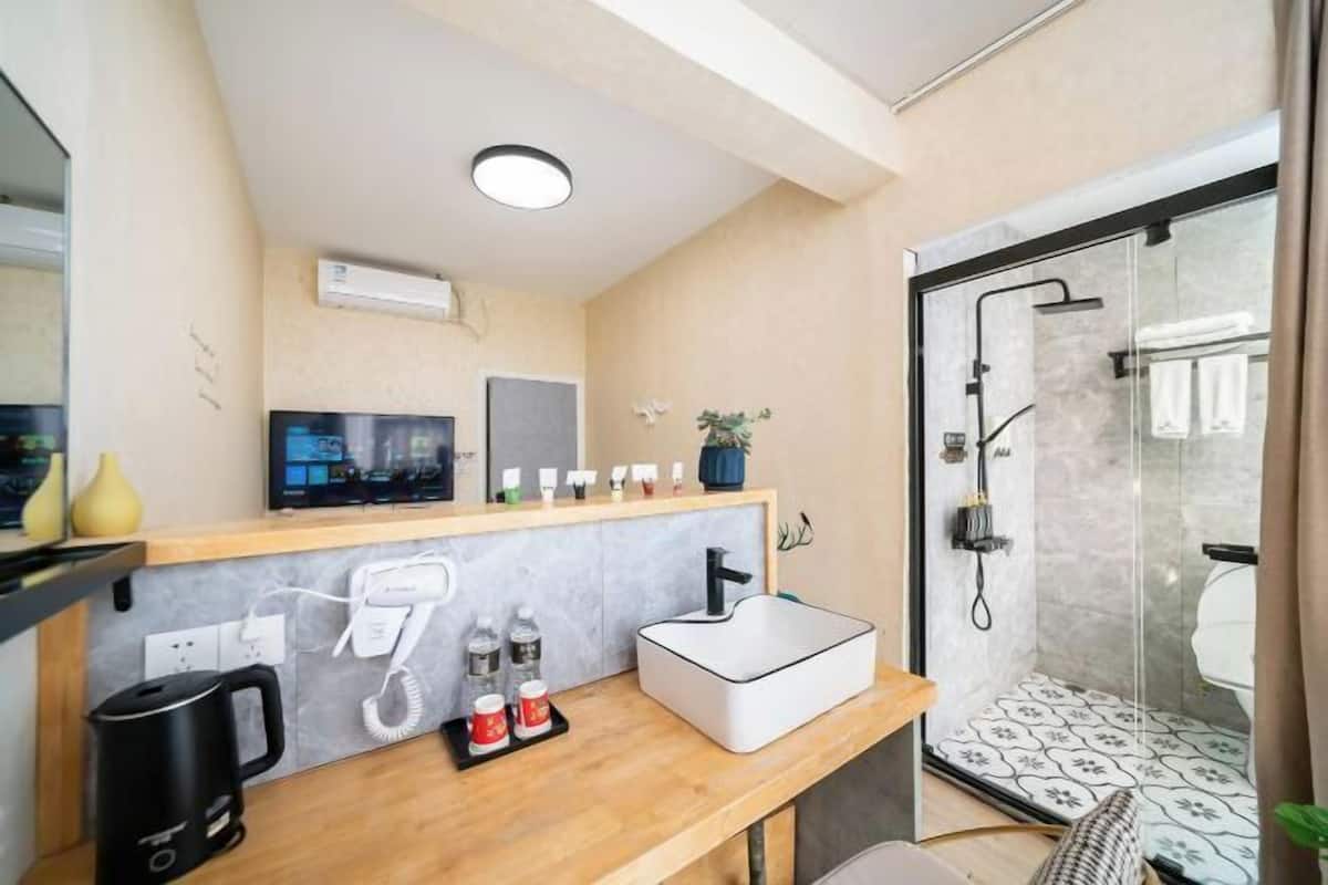 Un baño moderno con ducha, lavamanos, cafetera y televisor en la pared.