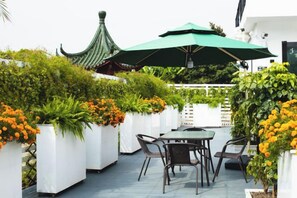 An outdoor patio with a table and chairs, surrounded by white planters with orange flowers, and a green umbrella providing shade. - Shanghai Qichi homestay (Shanghai)