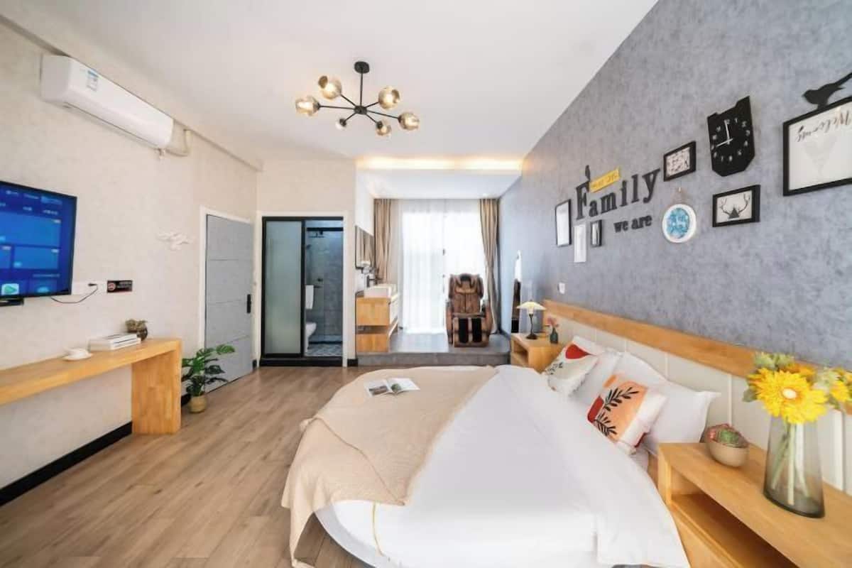 Habitación de hotel con cama, mesitas de noche, televisor, escritorio, silla y una pared decorada con cuadros y un reloj.