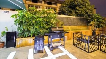 An outdoor patio area with a grill, potted plants, and a seating area.