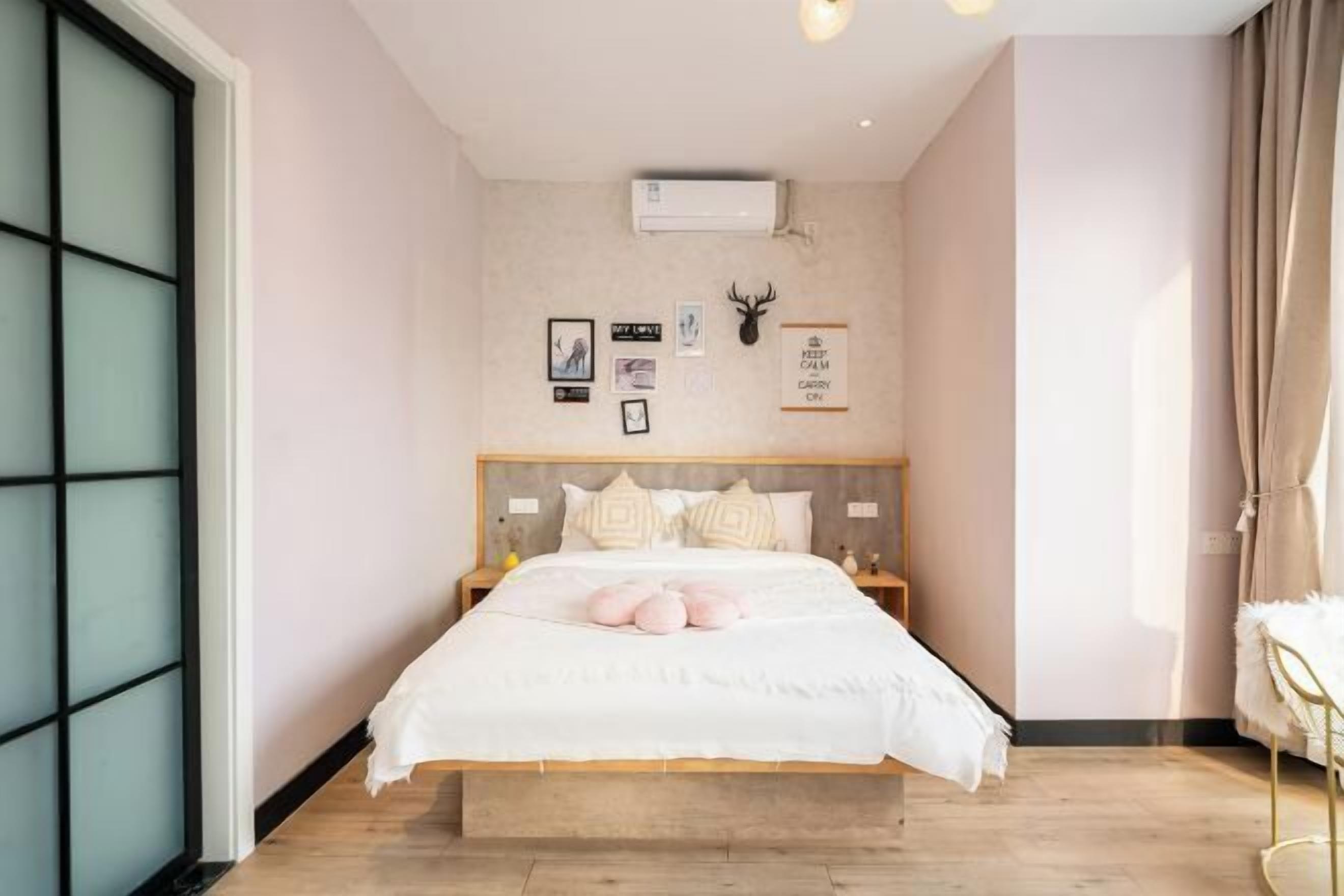 A bedroom with a bed, a headboard, a wall-mounted air conditioner, and a window with a curtain.