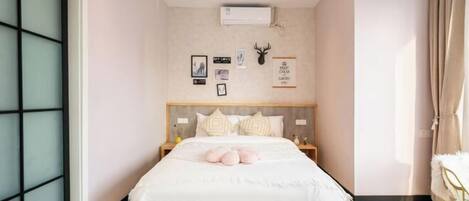 A bedroom with a bed, a headboard, a wall-mounted air conditioner, and a window with a curtain.