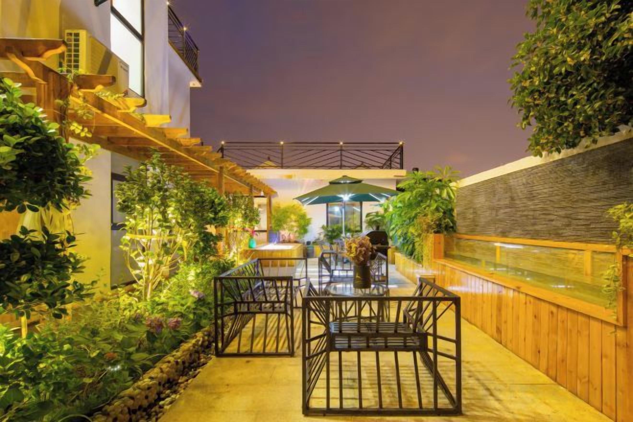 An outdoor dining area with a table and chairs, surrounded by plants and a wooden fence.
