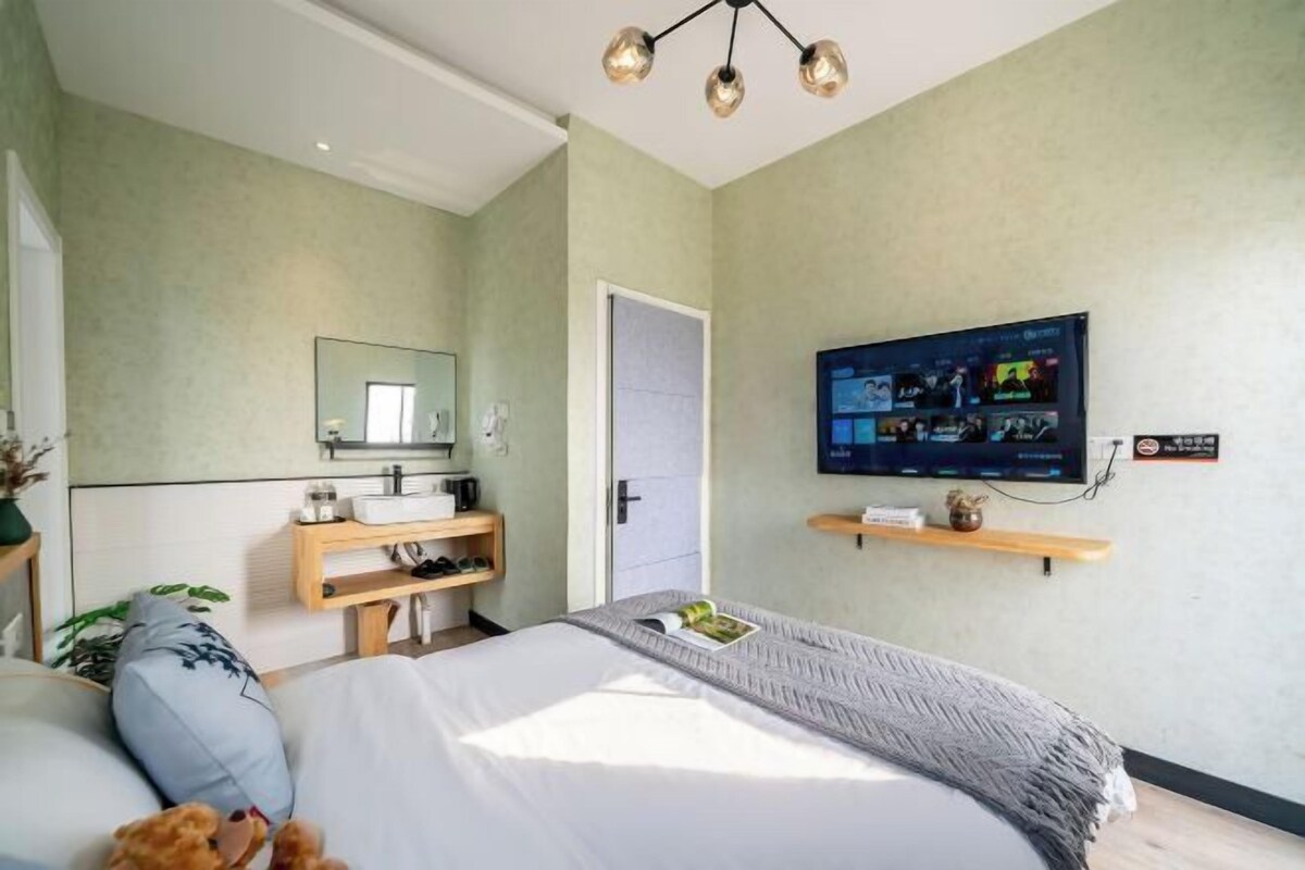 A modern hotel room with a bed, a television mounted on the wall, a mirror, and a wooden shelf with a plant.