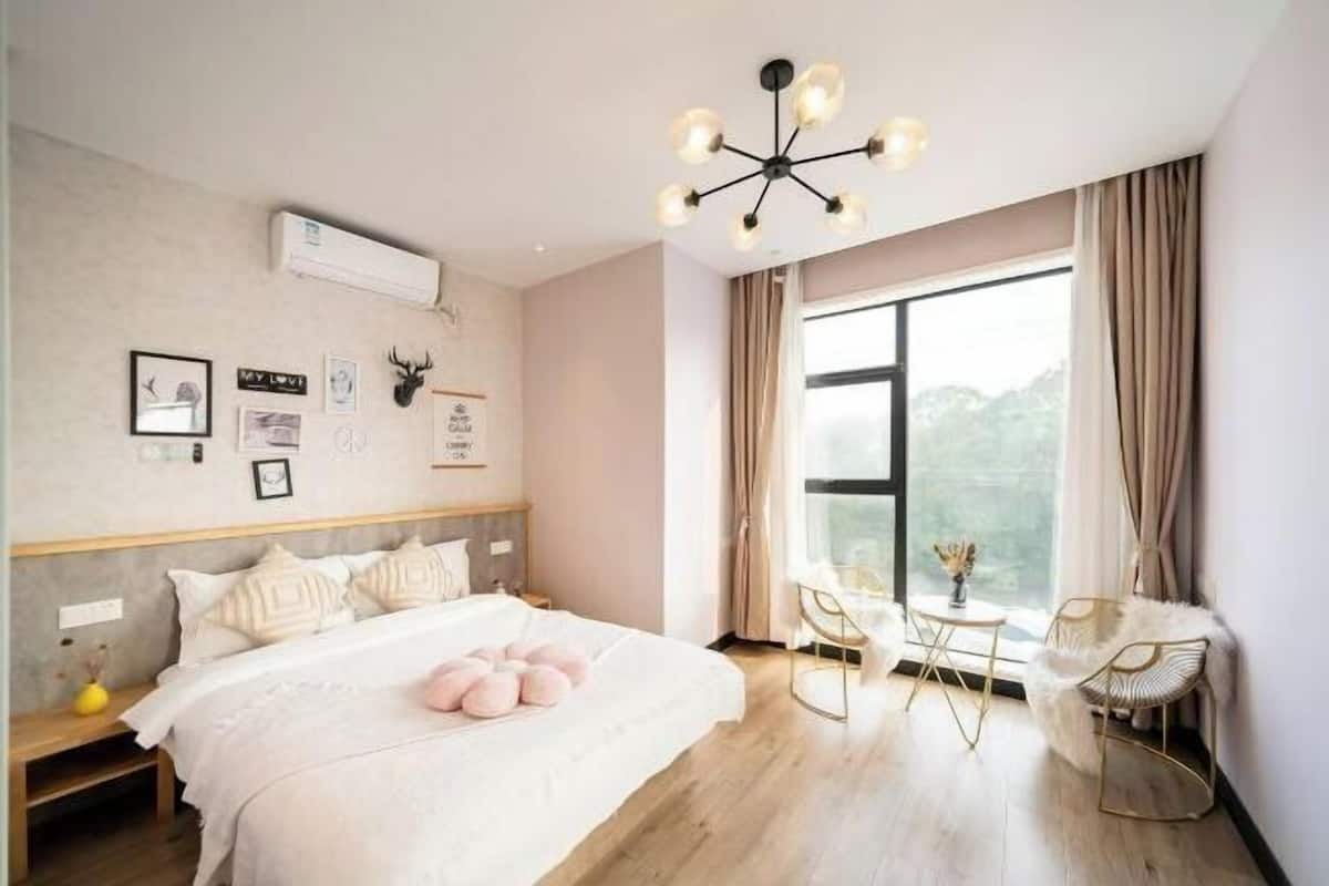 Un dormitorio con cama, una araña, una ventana con cortinas y una pequeña mesa con sillas.