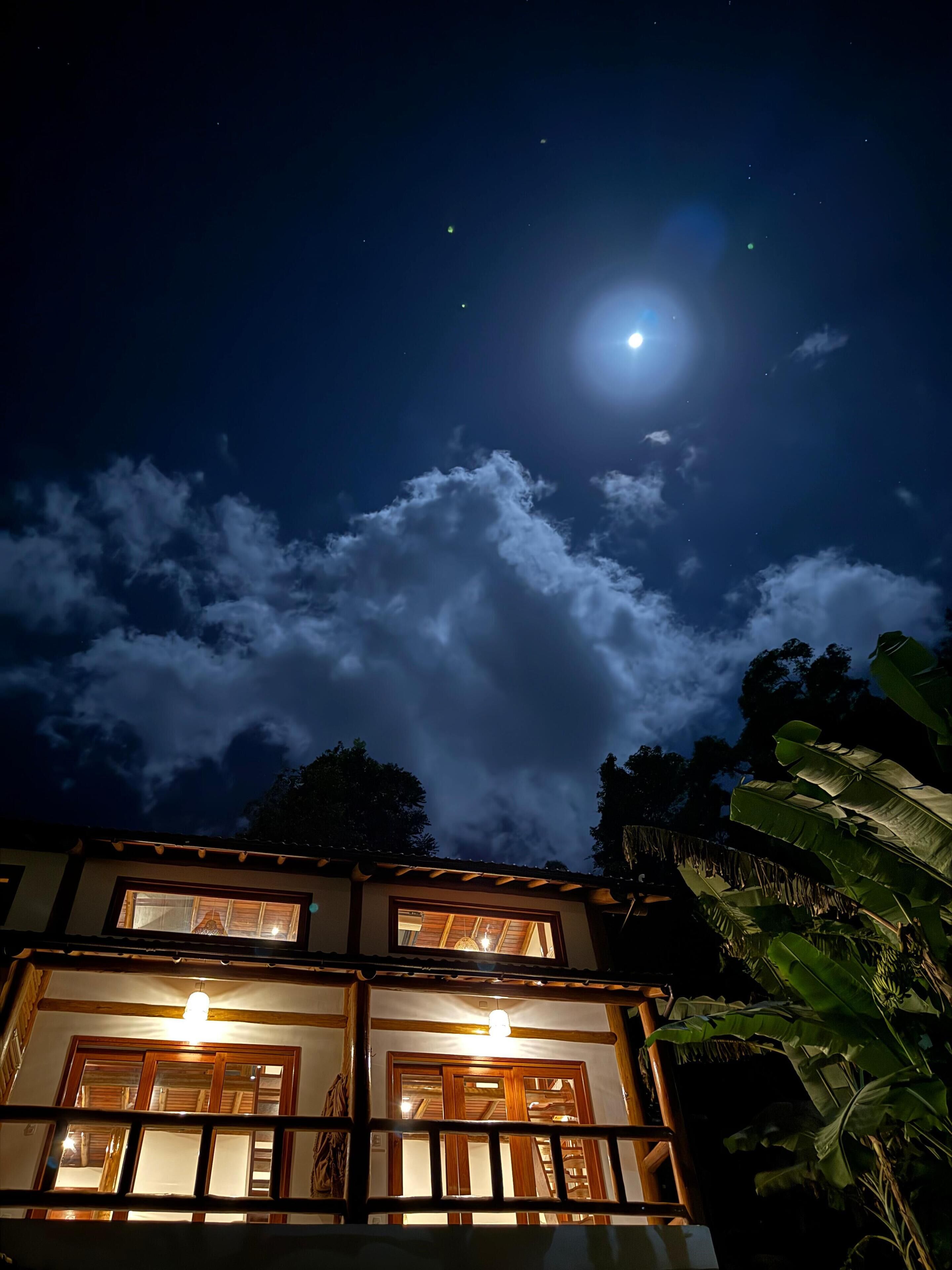 Un edificio con varias ventanas y un balcón, bajo un cielo nocturno con luna y nubes.