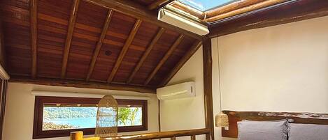Un dormitorio con techo de madera, una cama con ropa de cama blanca, una ventana con vistas y un pequeño balcón con barandilla de madera.