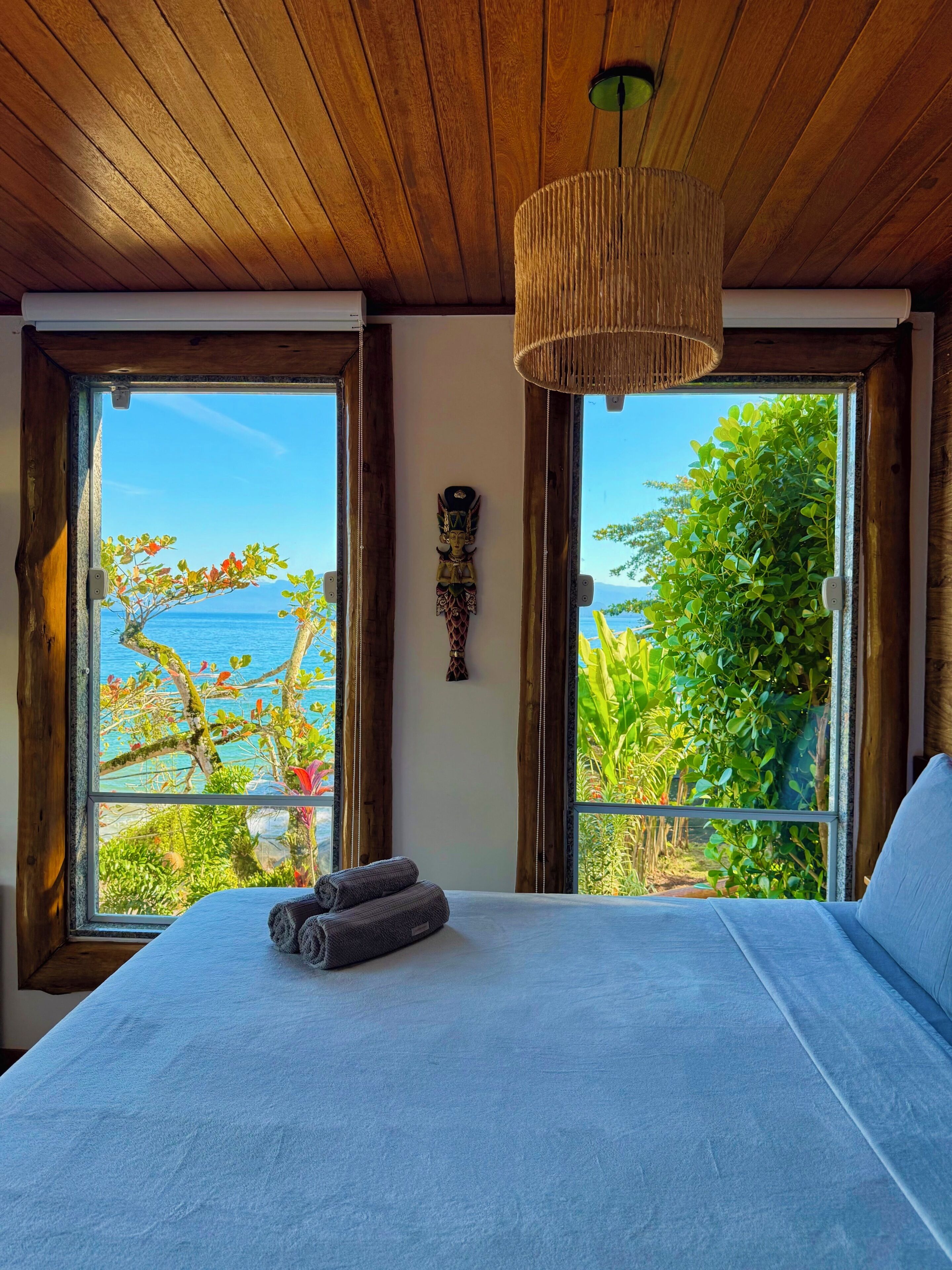 Un dormitorio con una cama grande, techo de madera y vista al mar a través de amplios ventanales.