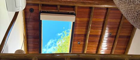 Techo de madera con tragaluces, una lámpara de fibra y vista a la vegetación exterior.