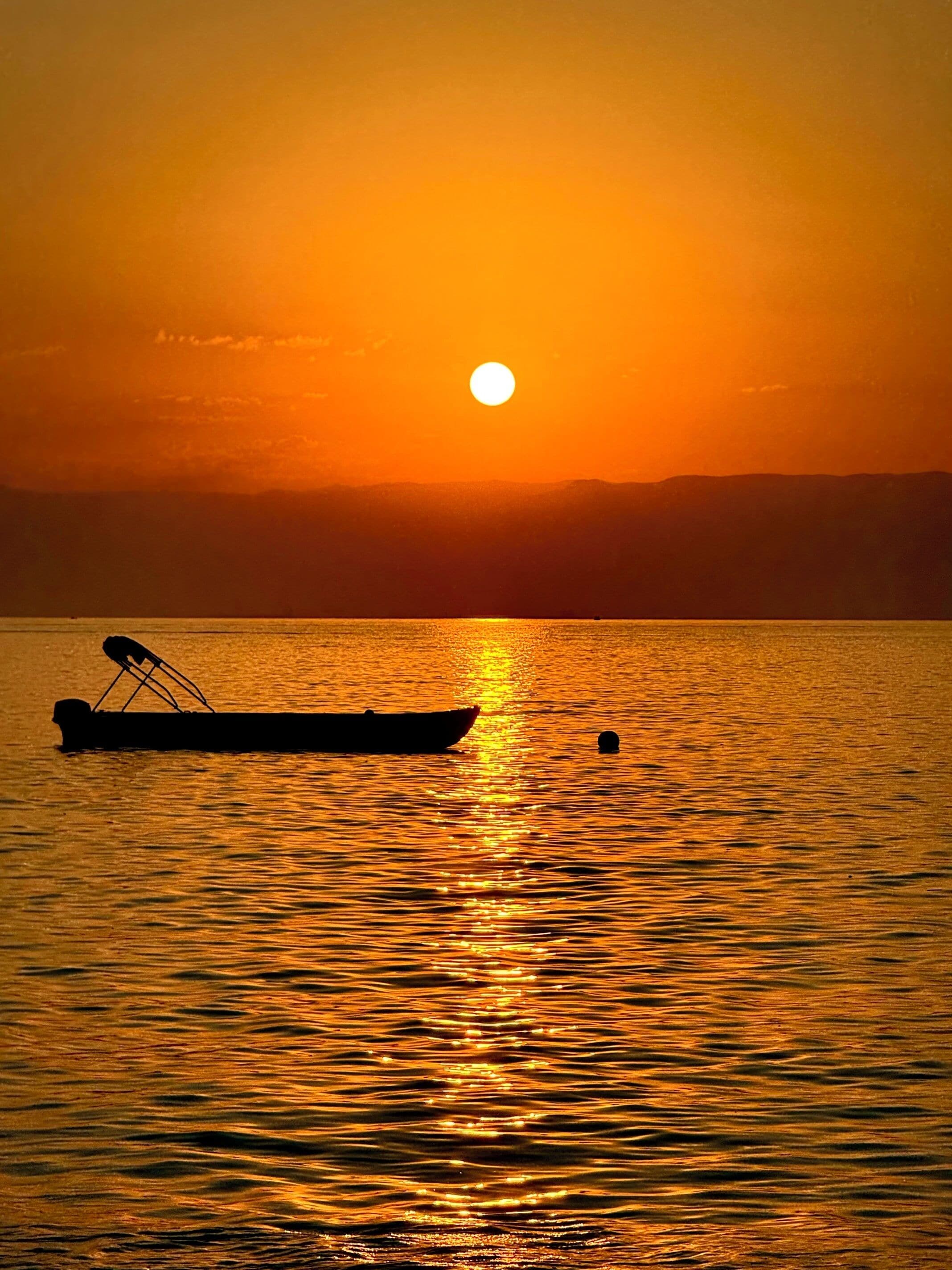 Een boot op kalm water, de zonsondergang wordt erin weergegeven.