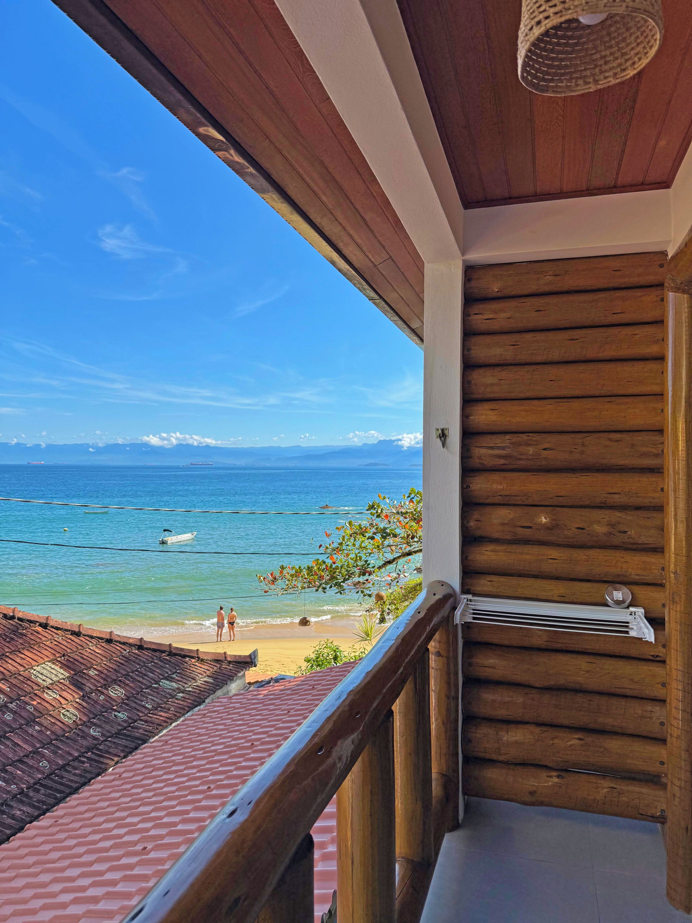A wooden balcony with a view of the beach and ocean.